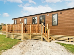 A wooden building with a fenced deck, a staircase, and a gravel driveway. - Hedgehog Lodge (Carnforth)