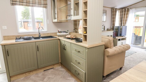 A compact kitchen with a sink, cabinets, and a dining area with a table and sofa. - Hedgehog Lodge (Carnforth)