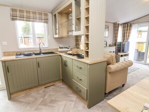 A compact kitchen with a sink, cabinets, and a dining area with a table and sofa. - Hedgehog Lodge (Carnforth)