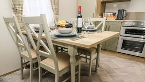 A dining area with a wooden table, chairs, and a kitchen in the background. - Hedgehog Lodge (Carnforth)