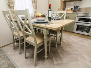 A dining area with a wooden table, chairs, and a kitchen in the background. - Hedgehog Lodge (Carnforth)