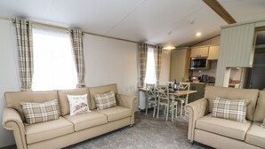 A living room with two beige sofas, a dining table, and a kitchen area. - Hedgehog Lodge (Carnforth)