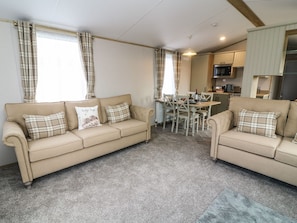 A living room with two beige sofas, a dining table, and a kitchen area. - Hedgehog Lodge (Carnforth)