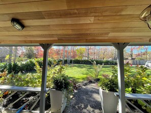 Un espacio al aire libre techado con un sendero de grava, plantas en macetas y vistas a un césped y árboles bien cuidados.