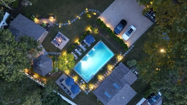 Vista aérea de una propiedad residencial con piscina, zona de patio y dos coches aparcados fuera.