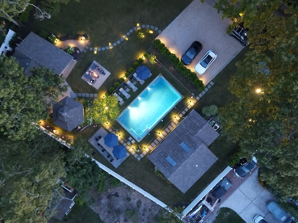 Eine Luftaufnahme eines Wohnhauses mit Schwimmbad, Terrasse und zwei geparkten Autos vor der Fassade.