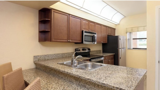 A kitchen with granite countertops, a stainless steel sink, a microwave, a stove, and wooden cabinets. - 2-bedroom resort suite in the heart of Orlando (Orlando)