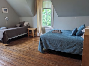 A bedroom with two beds, a small wooden table, a window with curtains, and a picture on the wall.