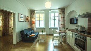 Ett kompakt bostadsutrymme med en soffa, ett matbord, stolar, en tv och ett litet kök.