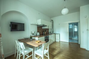 Una cocina moderna con una isla de madera, sillas blancas, un televisor de pantalla plana y una zona de ducha con mampara de vidrio.