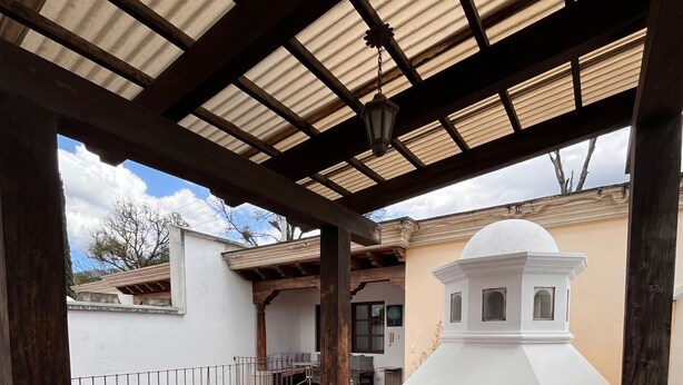 A covered patio with a glass table and chairs, terracotta tiles, and a white building with a dome in the background. - Casa Don Pancho (Ciudad Vieja)