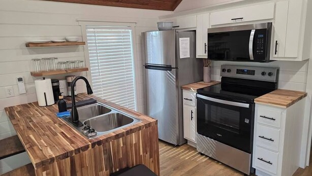 Cocina compacta con una isla de madera, electrodomésticos de acero inoxidable y muebles altos blancos.
