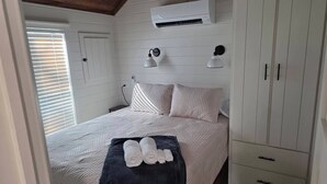 Un dormitorio con cama, armario blanco y aire acondicionado.