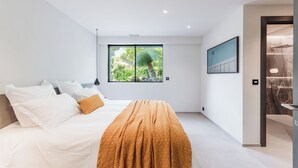 Een moderne slaapkamer met een groot bed, een raam met uitzicht op groen en een douche.