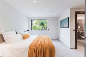 Ein modernes Schlafzimmer mit einem großen Bett, einem Fenster mit Blick auf Grünflächen und einem Duschbereich.