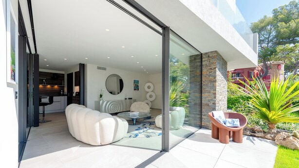Een modern interieur met een glazen deur naar een patio, een witte bank, een ronde salontafel en een accentmuur van natuursteen.