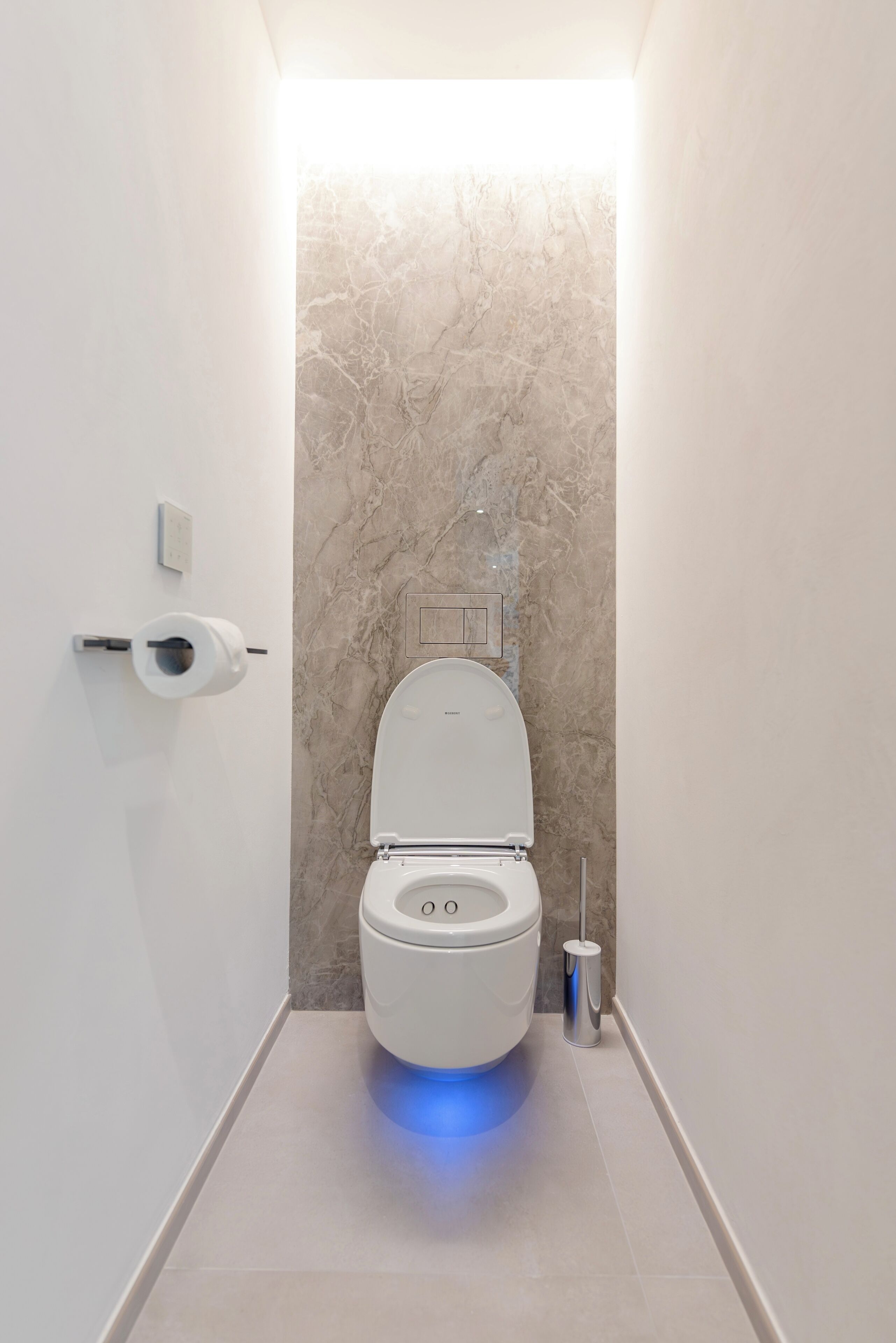 Ein modernes Badezimmer mit Toilette, Marmorwand und blau belebtem Boden.