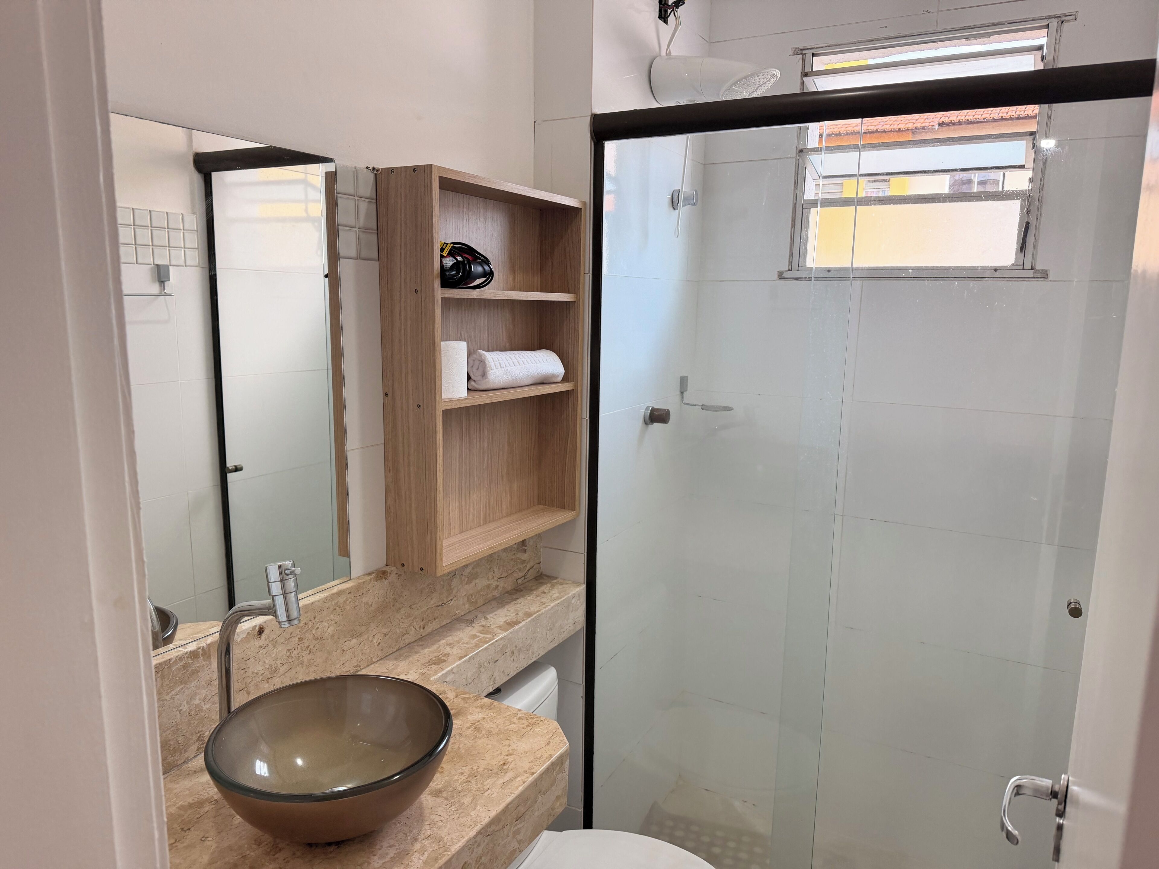 Une salle de bain avec un grand miroir, un lavabo en forme de coupe, une étagère en bois avec des serviettes et une douche à parois de verre.