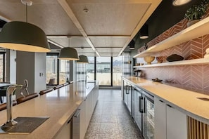 Eine moderne Küche mit einer langen Arbeitsplatte, Pendelleuchten und Blick durch das Fenster.