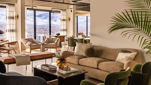 Ein modernes Wohnzimmer mit einer Couch, Sesseln, einem Couchtisch und Blick auf Berge durch große Fenster.