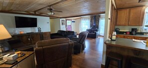 Ein Wohnzimmer mit Flachbildfernseher, Ledersofas, Holzboden und einer Küchenzeile mit Holzschränken und einer Bar.