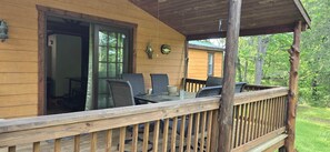 Eine Holzdielen-Terrasse mit Korbmöbeln, einem Glastür-Eingang und Blick auf ein bewaldetes Gebiet.