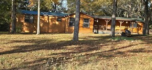Eine Hütte mit Veranda, umgeben von Bäumen und einer Wiese.
