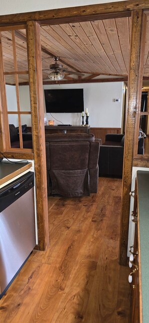 Ein Zimmer mit Holzrahmen, das eine Deckenventilator, einen Flachbildfernseher, ein Sofa und einen Essbereich mit Tisch und Stühlen bietet.