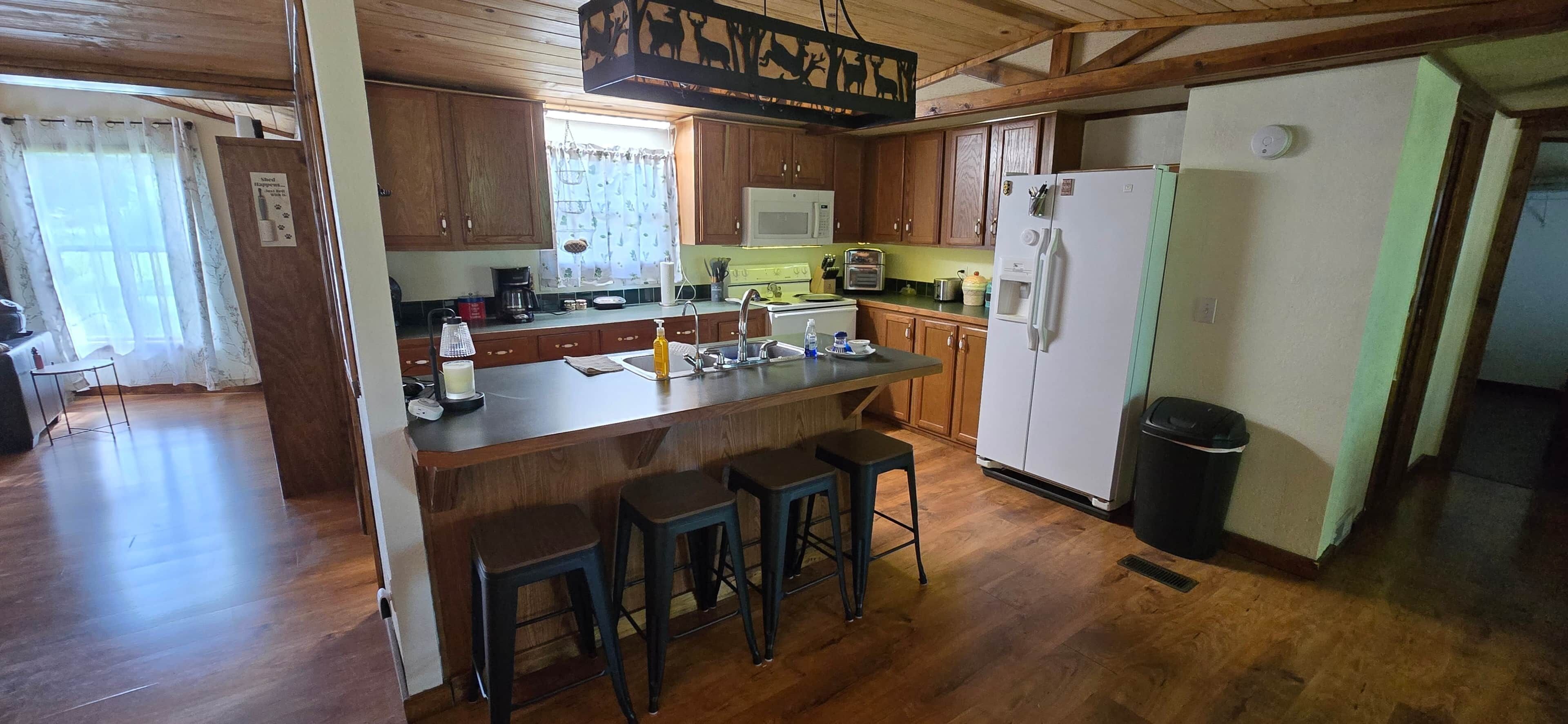 A kitchen with wooden cabinets, a central island with stools, a microwave, a toaster, and a refrigerator.