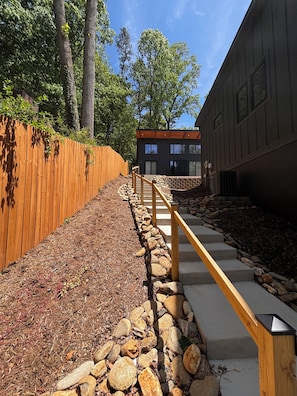 Un chemin menant à un bâtiment moderne, agrémenté d’une clôture en bois et de détails en pierre.
