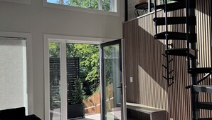 Ein großzügiger Wohnbereich mit großen Fenstern, einer modernen Treppe und einer Glastür zum Außenbereich.