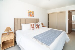 A bedroom with a bed, a nightstand with a lamp, a wall art piece, and a wardrobe. - Ocean View Condo Steps to Beach & Comfort (Jacó)