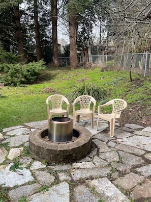 Un foyer en pierre, avec des chaises, aménagé dans un jardin.