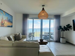 Un salón moderno con sofá, ventana grande y vista al mar.