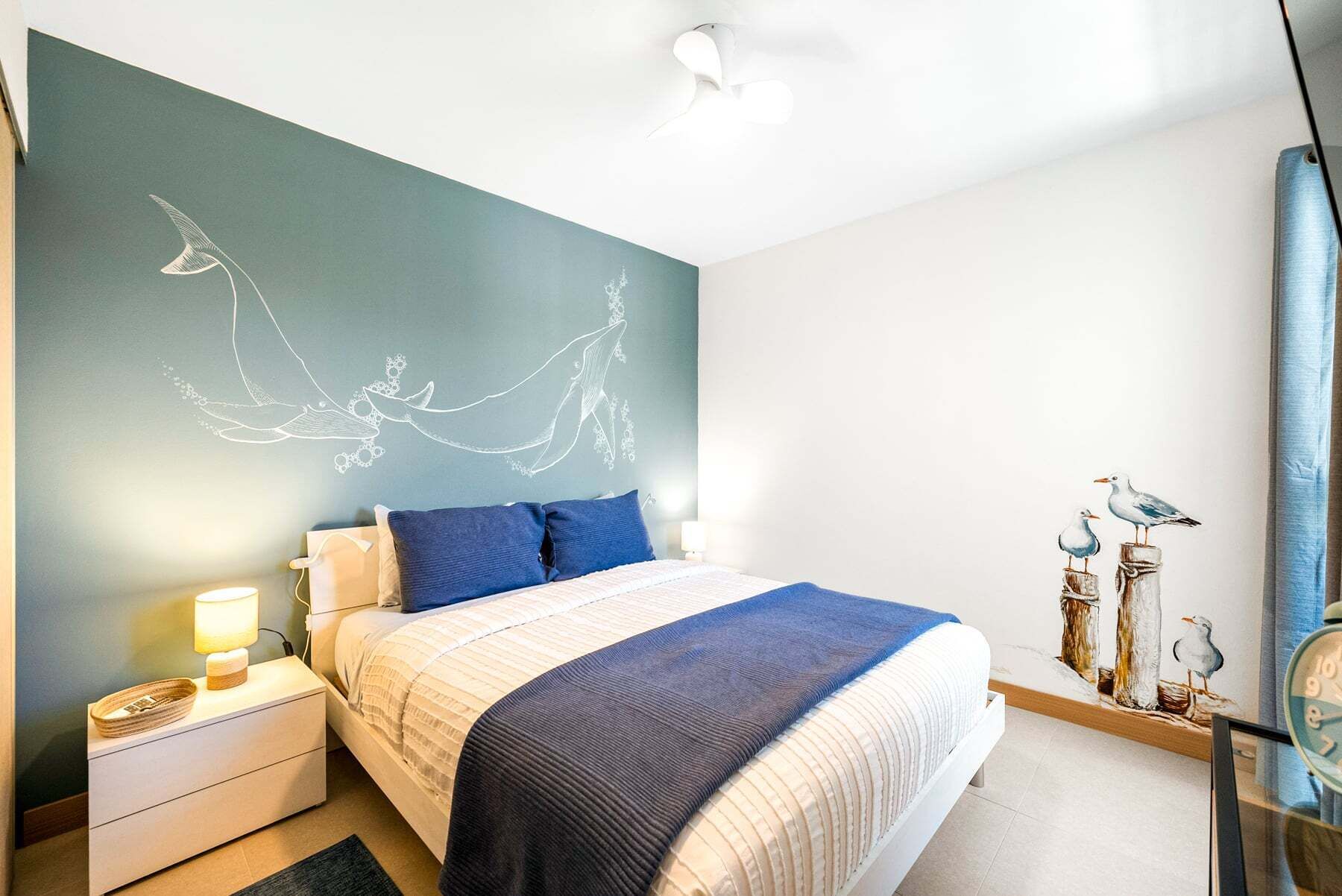 A bedroom with a bed, nightstand, lamp, and wall art.