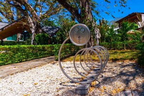 A metal sculpture with a bicycle symbol and a star, set in a garden with trees and a pathway. - Private Pool & Tropical Style, Minutes From the Beach (Jacó)