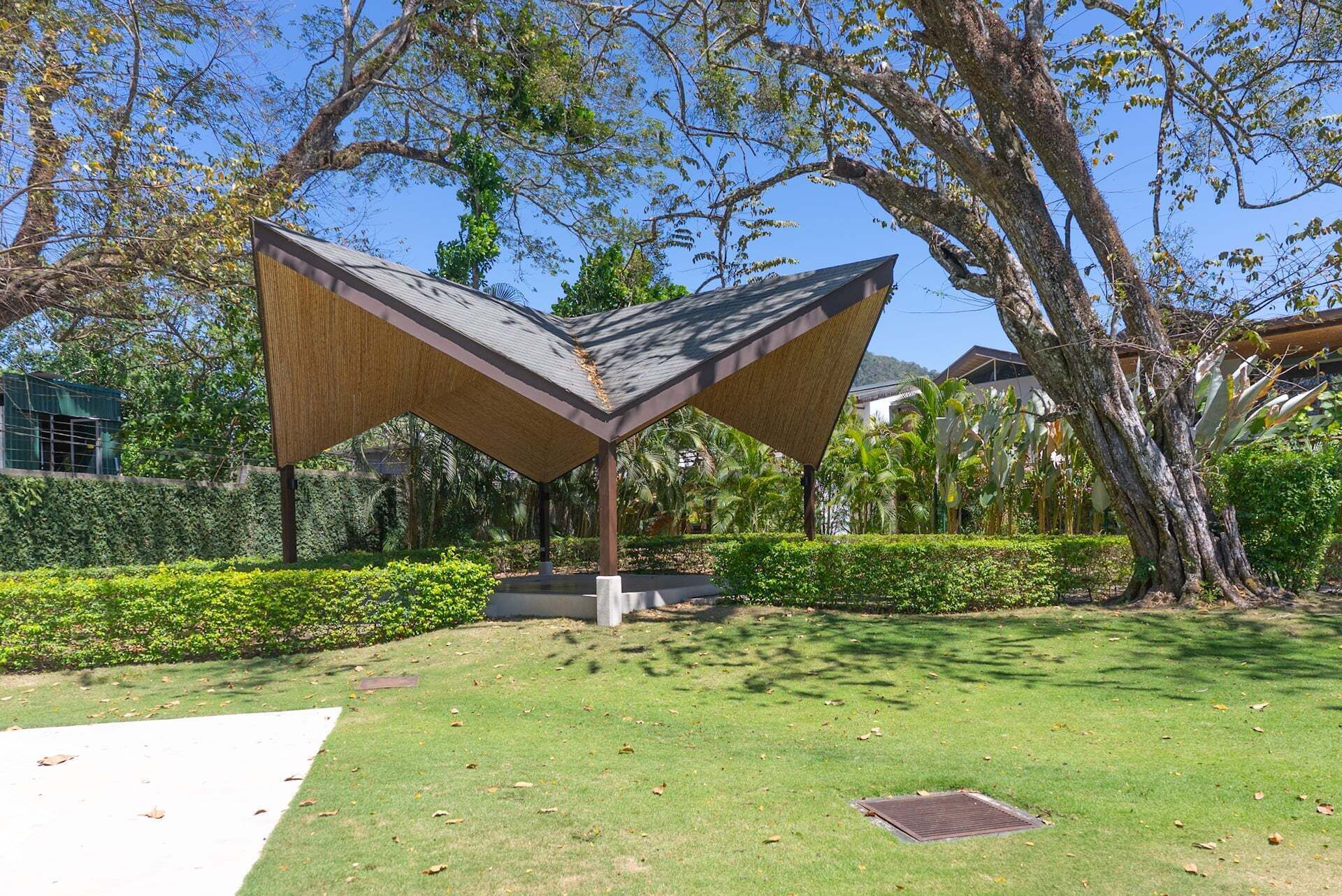 A modern pavilion structure with a geometric roof design, surrounded by well-maintained greenery and trees.