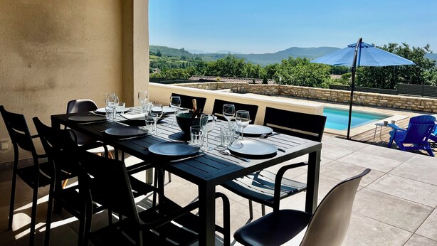 Un espace de restauration en plein air avec une table dressée pour quatre personnes, offrant une vue sur une piscine et un paysage pittoresque.
