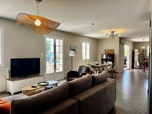 Ein modernes Wohnzimmer mit Fernseher, Sofa, Esstisch und Küchenbereich.