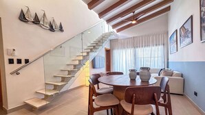Ein modernes Interieur mit einer Wendeltreppe, einem Essbereich mit rundem Tisch und Stühlen sowie einem Wohnbereich mit einer Couch und einem großen Fenster.