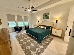 Une chambre à coucher avec un lit, un ventilateur de plafond, une table de chevet, une chaise et une fenêtre.