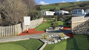 A golf course with a wooden fence, a signboard, and mobile homes in the background. - 26 Ocean View (Llwyngwril)