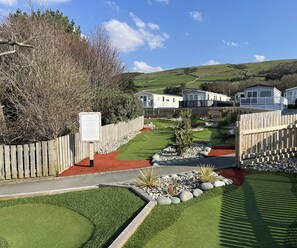 Um campo de golfe com cerca de madeira, uma placa e casas móveis ao fundo.