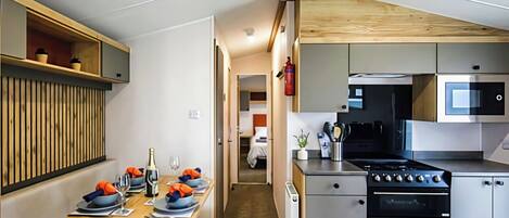 A compact kitchen with modern appliances, a dining area with a bench, and a visible hallway leading to a bedroom.