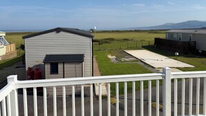 A caravan park with a metal shed, a fenced area, and a view of the sea and hills. - 26 Ocean View (Llwyngwril)