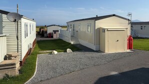 A row of mobile homes with a gravel driveway, a satellite dish, and a small shed. - 26 Ocean View (Llwyngwril)