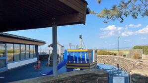 A children's play area with a slide and climbing structures, a covered seating area, and a stone wall. - 26 Ocean View (Llwyngwril)