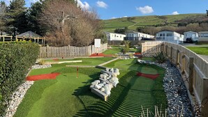 A campground with mobile homes, a fenced play area, and a hilly landscape in the background. - 26 Ocean View (Llwyngwril)