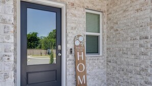Een huis met een donkere voordeur, een raam en een bord waarop staat 'Welcome to our HOME'.