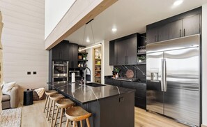 Une cuisine moderne dotée d’un îlot central, d’appareils électroménagers en acier inoxydable et de tabourets de bar en bois.